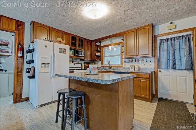 1962 Lake Pointe Dr, Ortonville, MI 48462 - kitchen with white appliances, light wood-style floors, a textured ceiling, a kitchen breakfast bar, and a center island