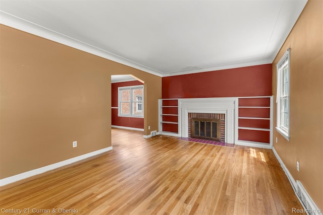711 N Highland St, Dearborn, MI 48128 - unfurnished living room featuring light wood-style flooring, arched walkways, a brick fireplace, and ornamental molding