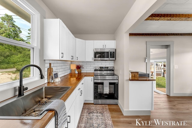12230 Mac Dr NE, Belding, MI 48809 - kitchen with appliances with stainless steel finishes, healthy amount of natural light, tasteful backsplash, white cabinetry, and beam ceiling