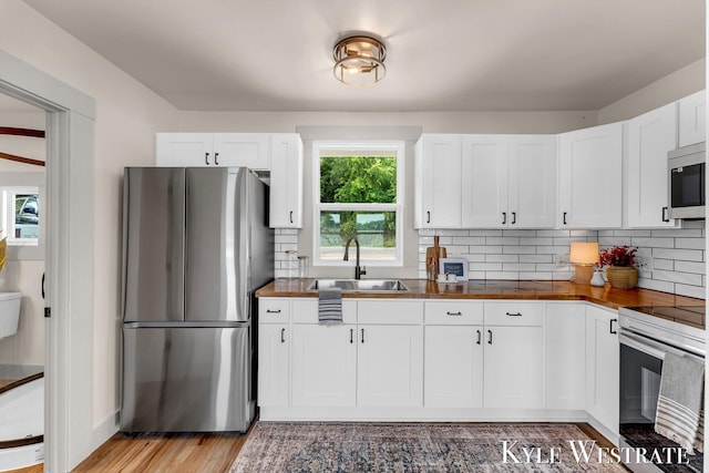 12230 Mac Dr NE, Belding, MI 48809 - kitchen with appliances with stainless steel finishes, white cabinets, tasteful backsplash, and light wood finished floors