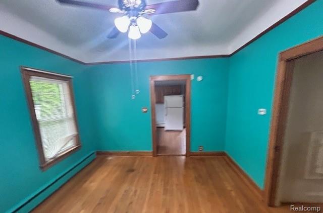 2170 Avondale St, Sylvan Lake, MI 48320 - spare room featuring baseboard heating, wood finished floors, and a ceiling fan