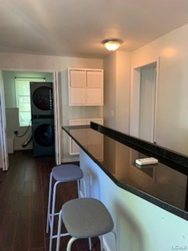 609 Orchard Ln, Tecumseh, MI 49286 - kitchen with estacked washer and dryer, dark wood-style floors, a breakfast bar area, dark countertops, and white cabinetry
