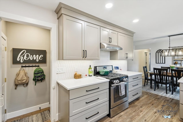 2641 Garfield Ave NW, Grand Rapids, MI 49544 - kitchen with gas stove, under cabinet range hood, gray cabinetry, light wood finished floors, and decorative backsplash