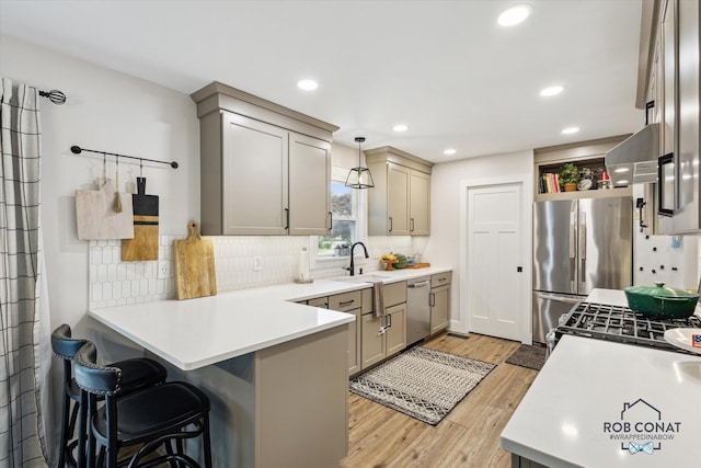 2641 Garfield Ave NW, Grand Rapids, MI 49544 - kitchen featuring stainless steel appliances, a peninsula, light wood-style floors, tasteful backsplash, and a breakfast bar area