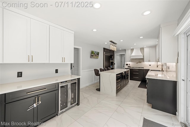 5534 Apple Ridge Trl, West Bloomfield, MI 48322 - kitchen with beverage cooler, premium range hood, white cabinets, a kitchen island, and light marble finish flooring