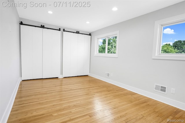 22222 Evergreen St, Macomb, MI 48082 - unfurnished bedroom with a barn door, light wood-style flooring, and recessed lighting