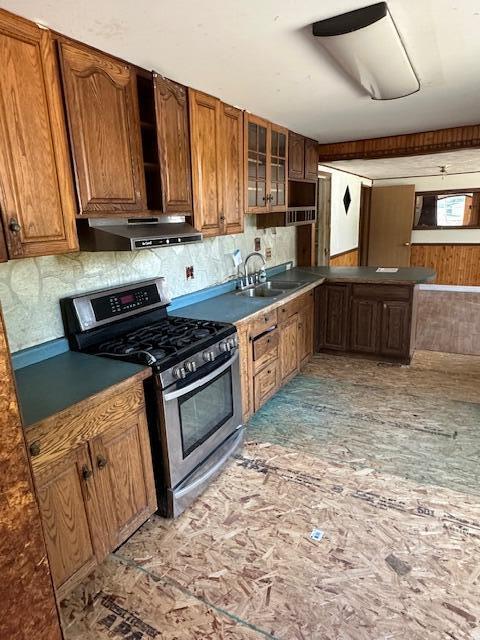 1675 E 8th St, White Cloud, MI 49349 - kitchen with stainless steel gas range oven, exhaust hood, brown cabinets, backsplash, and glass insert cabinets