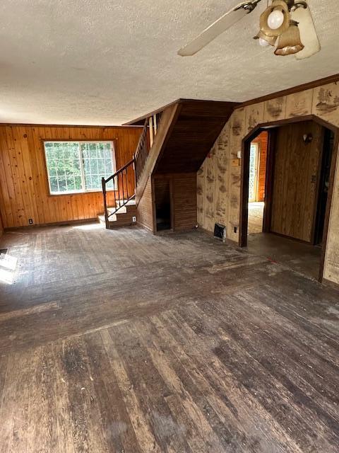 1675 E 8th St, White Cloud, MI 49349 - unfurnished living room featuring hardwood / wood-style flooring, wooden walls, stairway, arched walkways, and a textured ceiling