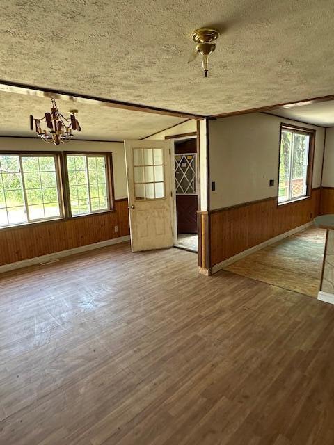 1675 E 8th St, White Cloud, MI 49349 - unfurnished room featuring a textured ceiling, wood walls, wood finished floors, a wainscoted wall, and a chandelier