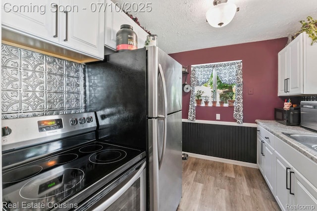 135 Bevins St, Holly, MI 48442 - kitchen with stainless steel range with electric cooktop, black microwave, light wood-style floors, white cabinets, and a wainscoted wall