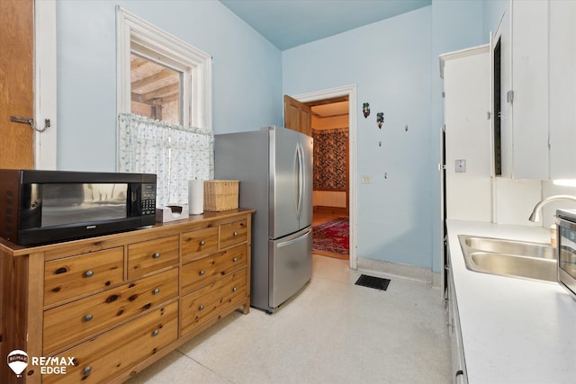 616 S Warren Ave, Saginaw, MI 48607 - kitchen with freestanding refrigerator, black microwave, white cabinets, light countertops, and light floors
