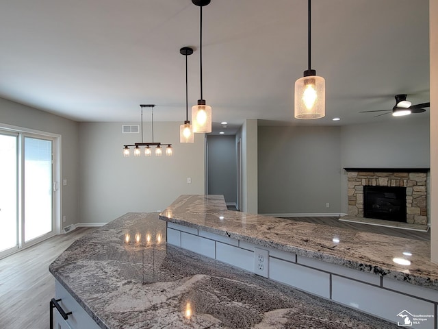 2844 1st St, Monroe, MI 48162 - kitchen featuring stone counters, ceiling fan, light wood-style floors, a stone fireplace, and hanging light fixtures