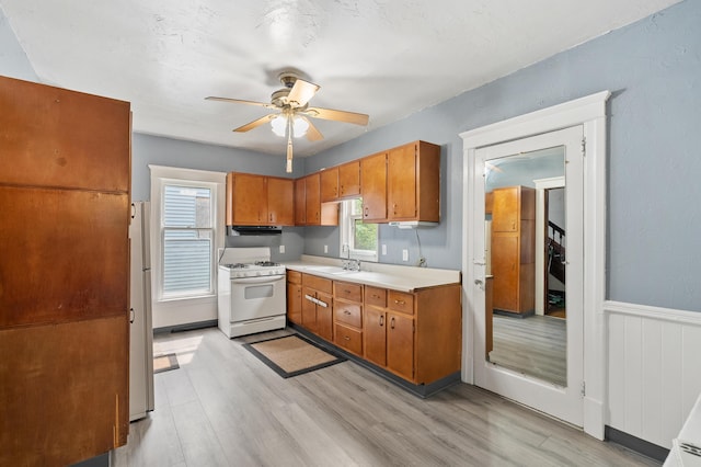 1310 Washington Ave, Kalamazoo, MI 49001 - kitchen featuring white appliances, light wood finished floors, brown cabinetry, ceiling fan, and light countertops