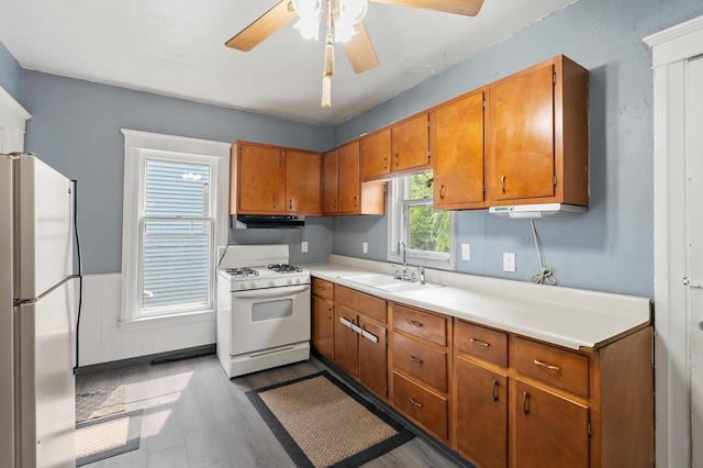1310 Washington Ave, Kalamazoo, MI 49001 - kitchen with white appliances, brown cabinetry, a ceiling fan, light countertops, and under cabinet range hood