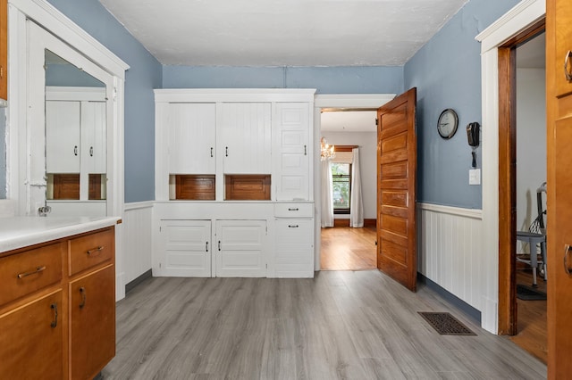 1310 Washington Ave, Kalamazoo, MI 49001 - kitchen with a wainscoted wall, light wood finished floors, light countertops, a chandelier, and brown cabinets
