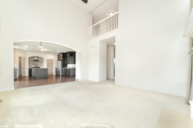 4215 Chandi Ct, Ypsilanti, MI 48197 - unfurnished living room featuring dark carpet, arched walkways, a high ceiling, and a ceiling fan