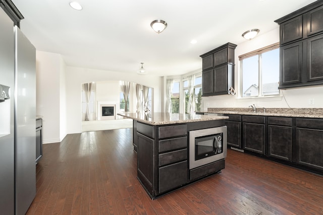 4215 Chandi Ct, Ypsilanti, MI 48197 - kitchen with appliances with stainless steel finishes, a glass covered fireplace, open floor plan, light stone countertops, and dark wood-style flooring