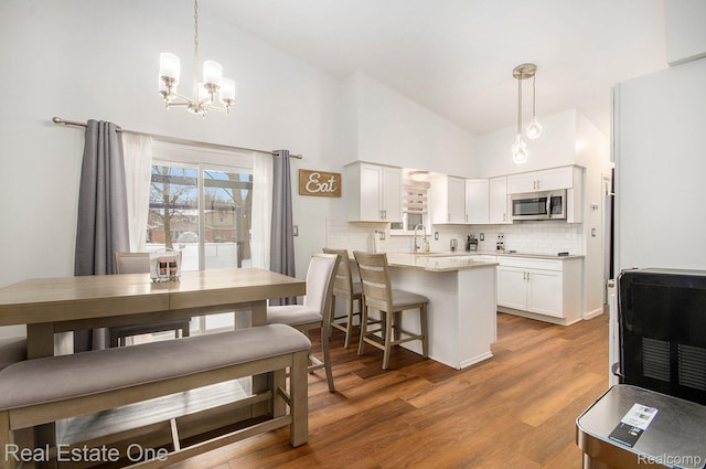 8477 Church Rd, Grosse Ile, MI 48138 - kitchen with stainless steel microwave, a chandelier, a peninsula, tasteful backsplash, and white cabinetry