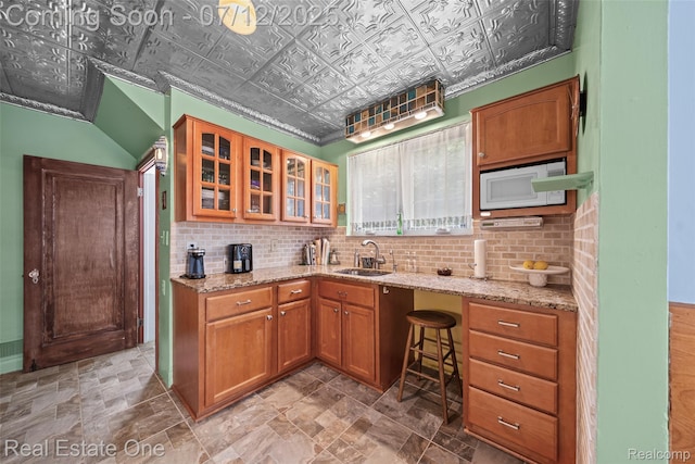 115 Illinois Ave, Pontiac, MI 48341 - kitchen featuring white microwave, an ornate ceiling, light stone counters, glass insert cabinets, and brown cabinetry