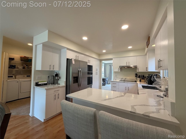 4178 Breckenridge Dr, West Bloomfield, MI 48322 - kitchen with black appliances, washer and dryer, a peninsula, under cabinet range hood, and light stone counters