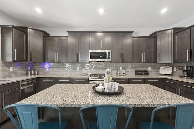 18734 Leonard Ct, New Buffalo, MI 49117 - kitchen featuring appliances with stainless steel finishes, a breakfast bar, dark brown cabinets, decorative backsplash, and a center island
