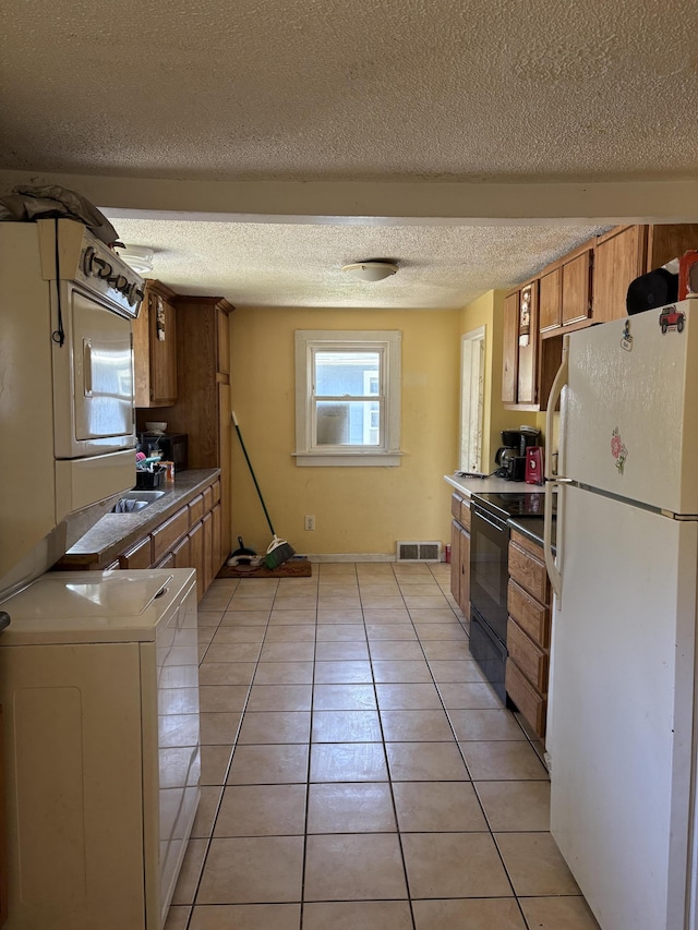 1993 Taube Ave, Benton Harbor, MI 49022 - kitchen with freestanding refrigerator, black electric range, washer / clothes dryer, light tile patterned flooring, and a textured ceiling