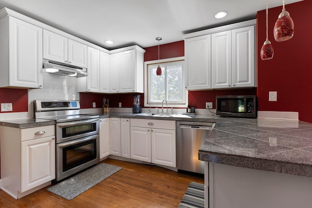 2017 Cumberland Dr, Brighton, MI 48114 - kitchen with stainless steel appliances, tile counters, under cabinet range hood, hanging light fixtures, and white cabinetry