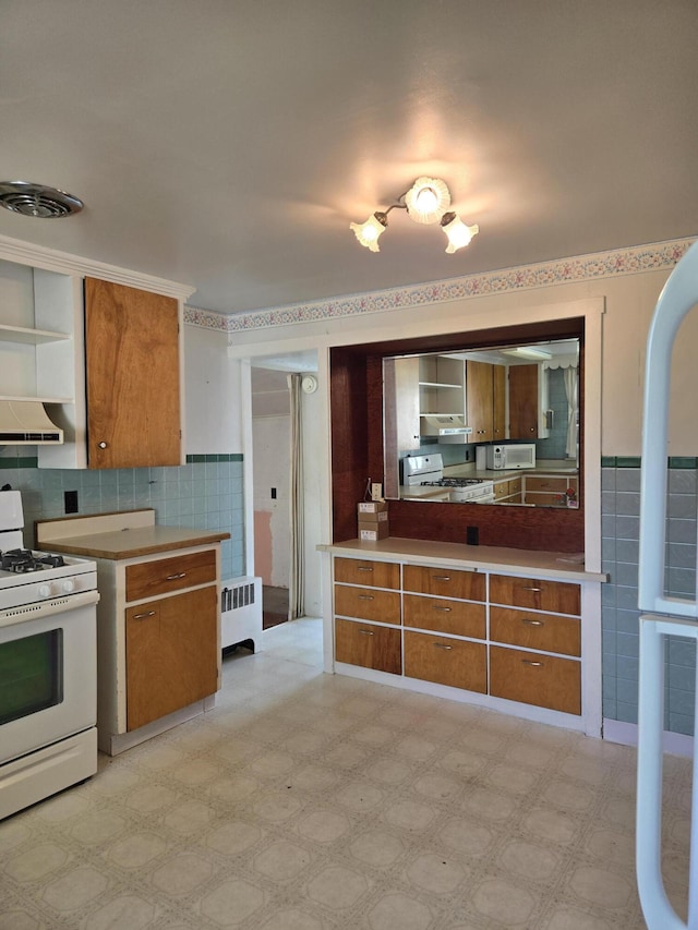 505 N Pine St, Evart, MI 49631 - kitchen with white appliances, radiator, brown cabinets, tile walls, and a wainscoted wall