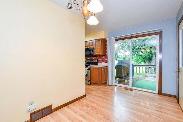 12345 Beadle Lake Rd, Battle Creek, MI 49014 - kitchen with stainless steel gas range oven, black microwave, a chandelier, and brown cabinetry