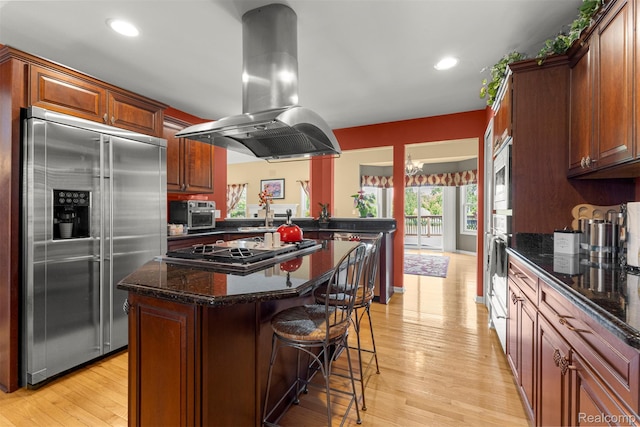 24065 Timber Creek Ln, Flat Rock, MI 48134 - kitchen featuring appliances with stainless steel finishes, island exhaust hood, a kitchen bar, light wood-style flooring, and a kitchen island