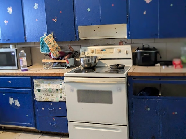 650 Pavone St, Benton Harbor, MI 49022 - kitchen with electric range, blue cabinets, stainless steel microwave, light tile patterned flooring, and tile counters