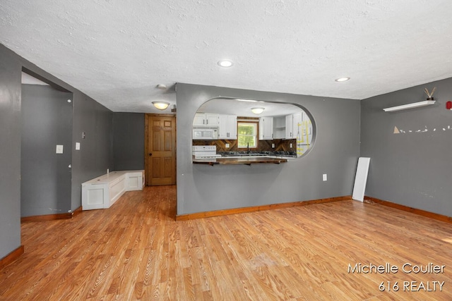 9583 E 5 Mile Rd, Big Rapids, MI 49307 - kitchen featuring white microwave, stove, a textured ceiling, white cabinetry, and light wood-style flooring