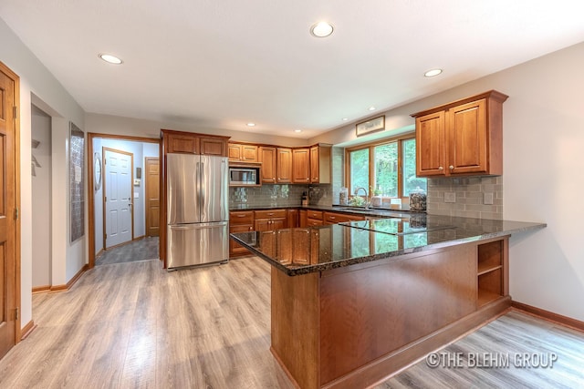 6340 Cannon Highlands Dr NE, Belmont, MI 49306 - kitchen with stainless steel appliances, brown cabinets, light wood-style flooring, dark stone countertops, and a peninsula