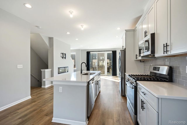 1087 Hampton Cir Unit 55, Detroit, MI 48207 - kitchen featuring appliances with stainless steel finishes, a kitchen island with sink, backsplash, dark wood-style floors, and light countertops