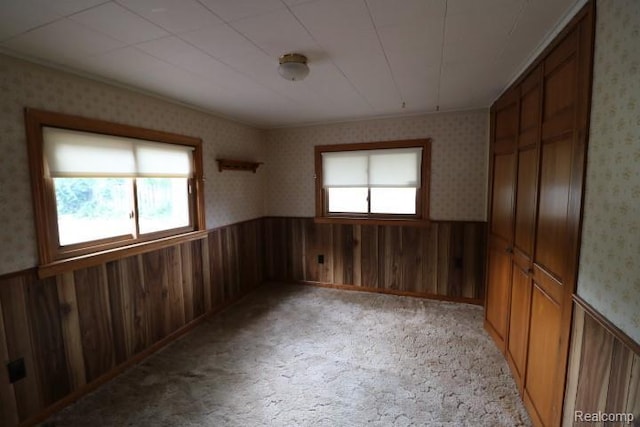 6048 N Lapeer Rd, Fostoria, MI 48435 - unfurnished bedroom featuring multiple windows, wainscoting, wallpapered walls, wood walls, and light colored carpet