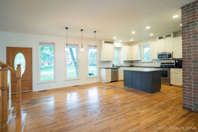 401 Erin Isle Ct, Holland, MI 49424 - kitchen featuring stainless steel appliances, light wood-type flooring, white cabinetry, a kitchen island, and decorative backsplash