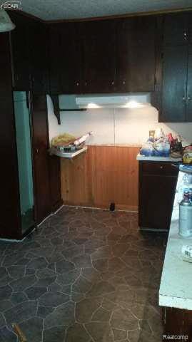 1702 Nebraska Ave, Flint, MI 48506 - kitchen featuring stone floors, light countertops, under cabinet range hood, and wood walls