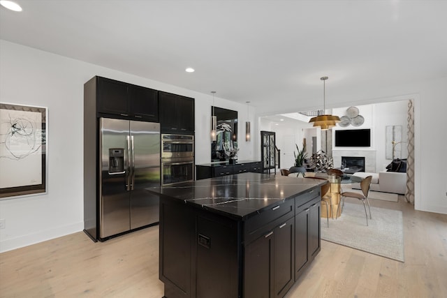 3909 Sandpiper Dr, Troy, MI 48083 - kitchen with stainless steel appliances, light wood-style floors, dark cabinetry, a kitchen island, and a glass covered fireplace