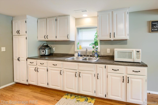 166 Indian Trl, Columbiaville, MI 48421 - kitchen featuring white microwave, dark countertops, white cabinets, and light wood-type flooring