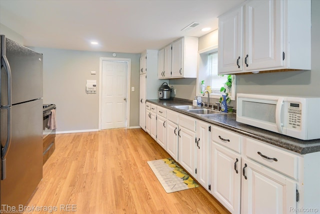 166 Indian Trl, Columbiaville, MI 48421 - kitchen featuring freestanding refrigerator, white microwave, light wood-style floors, dark countertops, and white cabinets
