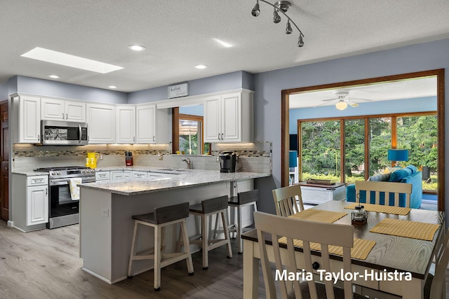 16205 Suffolk Dr, Spring Lake, MI 49456 - kitchen with appliances with stainless steel finishes, a peninsula, backsplash, white cabinetry, and a textured ceiling