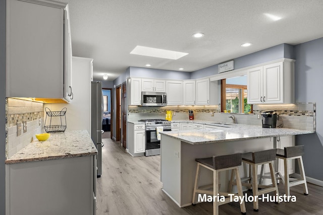 16205 Suffolk Dr, Spring Lake, MI 49456 - kitchen with appliances with stainless steel finishes, a skylight, a peninsula, tasteful backsplash, and a kitchen bar