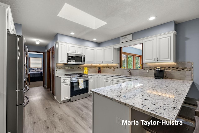 16205 Suffolk Dr, Spring Lake, MI 49456 - kitchen with stainless steel appliances, a skylight, a peninsula, white cabinetry, and recessed lighting