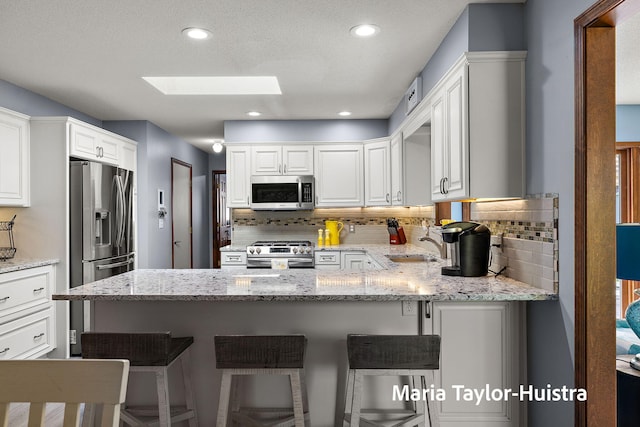 16205 Suffolk Dr, Spring Lake, MI 49456 - kitchen featuring stainless steel appliances, a skylight, tasteful backsplash, white cabinets, and recessed lighting