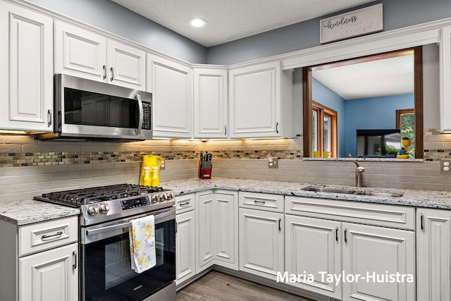 16205 Suffolk Dr, Spring Lake, MI 49456 - kitchen with appliances with stainless steel finishes, white cabinetry, backsplash, wood finished floors, and light stone counters