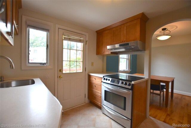 1983 Graefield Rd, Birmingham, MI 48009 - kitchen with stainless steel electric stove, under cabinet range hood, brown cabinetry, arched walkways, and light countertops