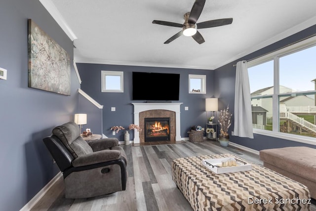 5845 Nile Dr SW, Wyoming, MI 49418 - living room featuring wood finished floors, a ceiling fan, a tiled fireplace, ornamental molding, and plenty of natural light