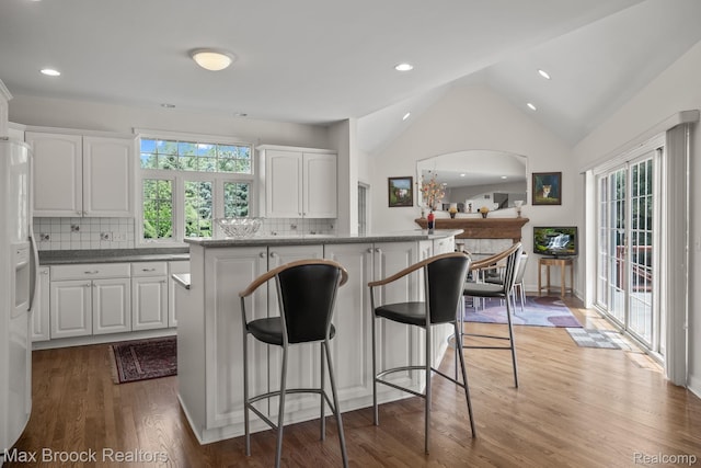 519 Hawksmoore Dr, Clarkston, MI 48348 - kitchen featuring white fridge with ice dispenser, wood finished floors, white cabinetry, a kitchen breakfast bar, and lofted ceiling