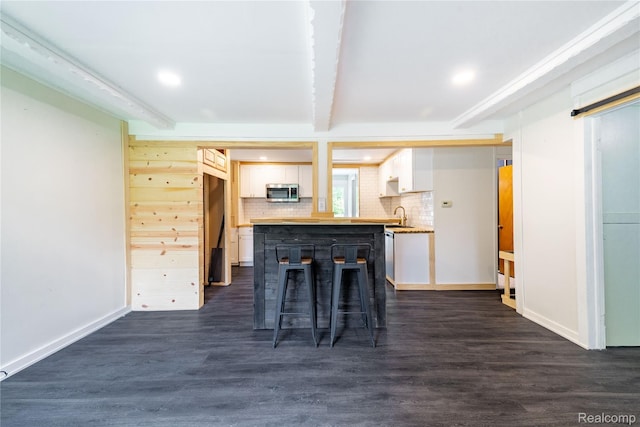 8614 Lake Rd, Grosse Ile, MI 48138 - kitchen with stainless steel microwave, white cabinetry, tasteful backsplash, dark wood-style flooring, and beam ceiling