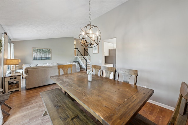 1393 Shankin Dr, Walled Lake, MI 48390 - dining room with lofted ceiling, stairway, light wood-style flooring, a chandelier, and a textured ceiling